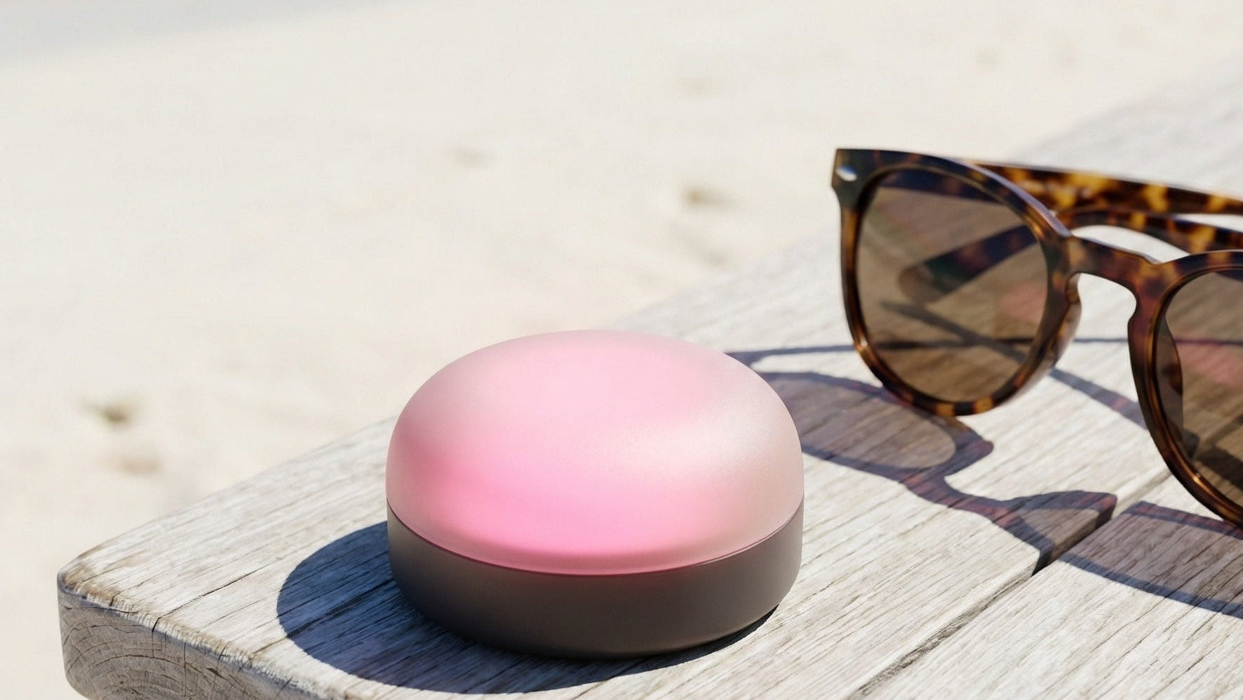 Pink and black device on a wooden surface with sunglasses in the background